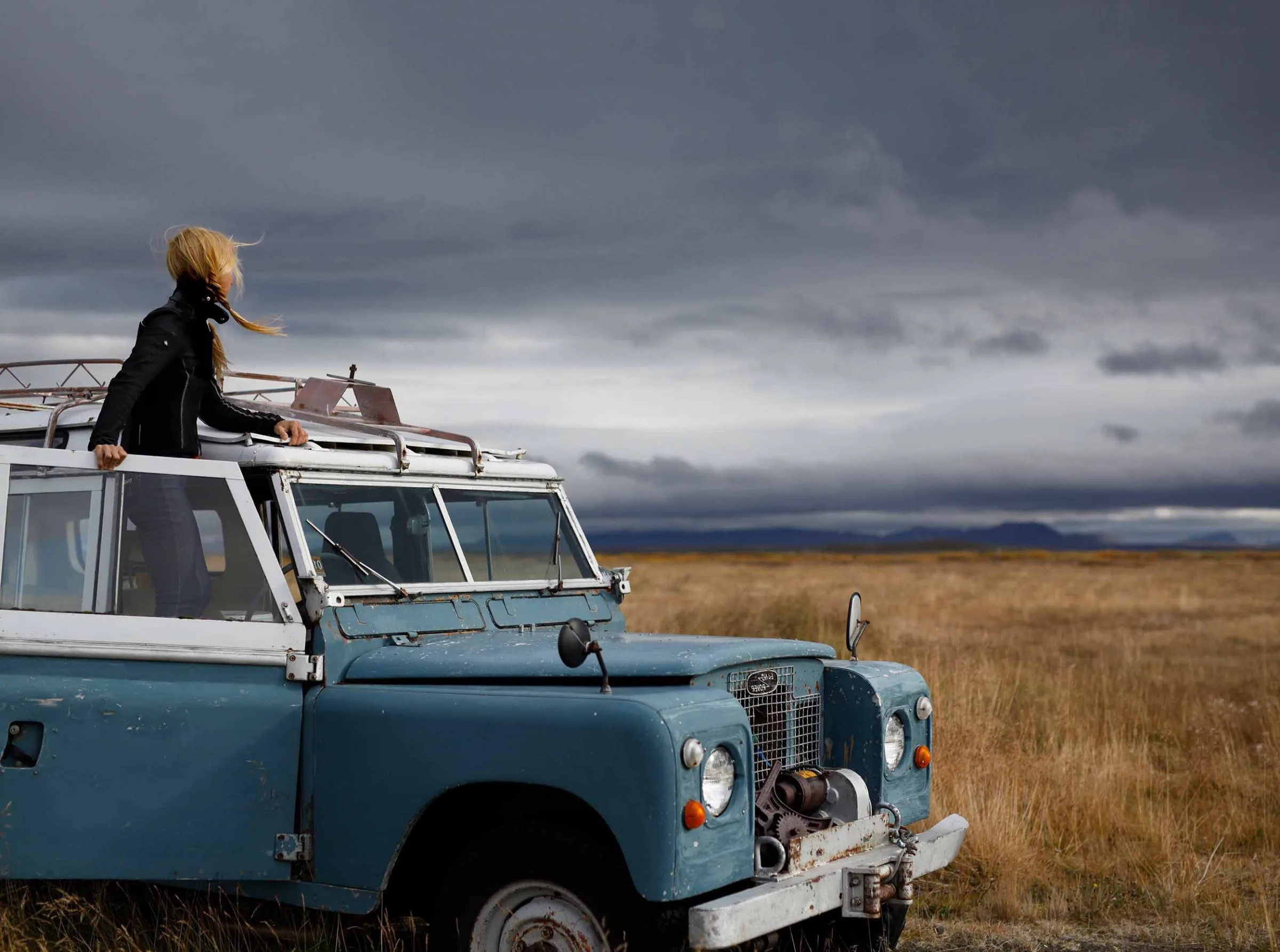Michelle on the roof of a vintage Land Rover under storm clouds in Iceland