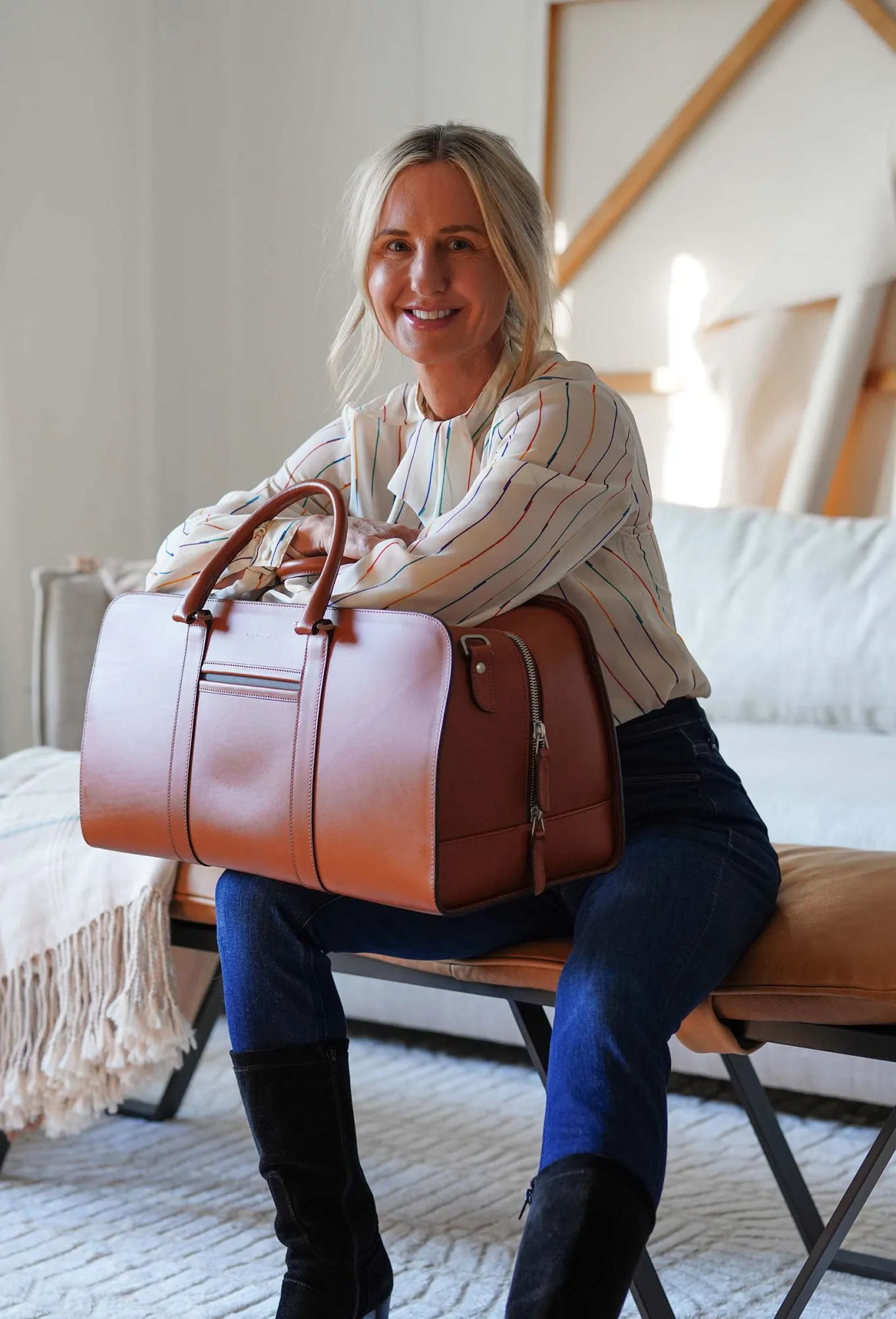 Michelle seated on a leather bench, smiling, with a cognac Carl Friedrik weekend bag
