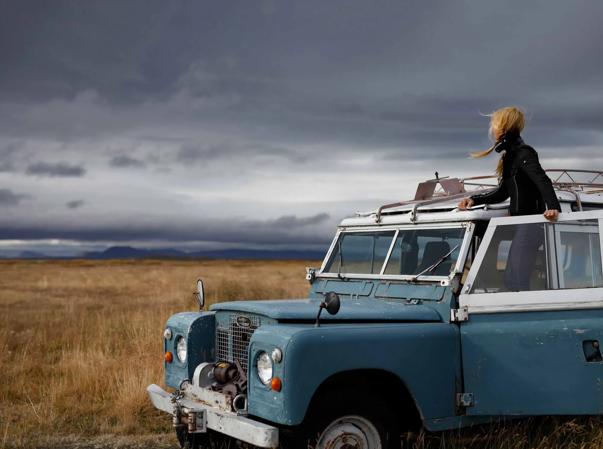 Sitting on the roof of a vintage pale-blue Land Rover under storm clouds in Iceland