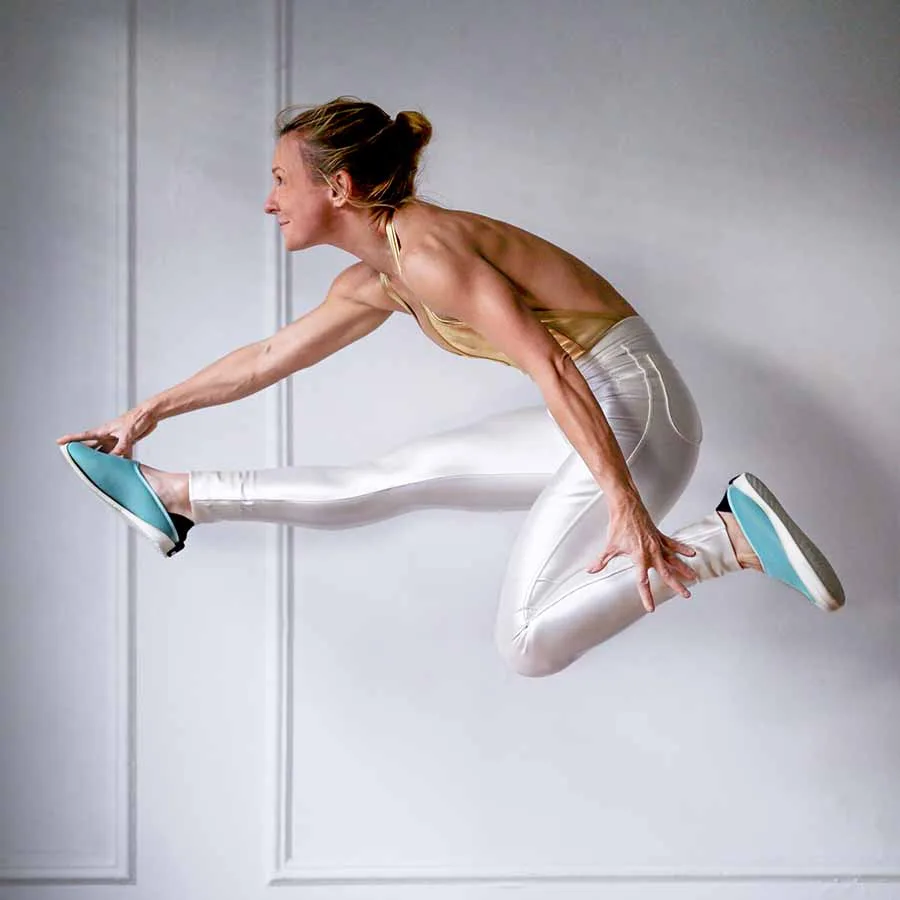 Split jump in blue Mahabis slippers in a white studio
